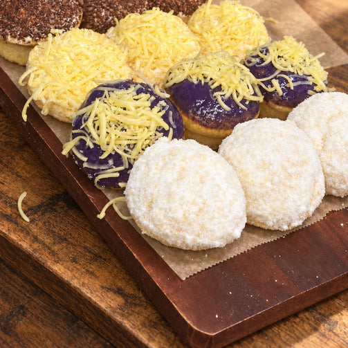 Assorted Max & Lucy's ensaymadas with classic, ube, queso de bola, and chocolate toppings on a wood board