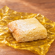 One unwrapped Max & Lucy's lemon square with powdered sugar on its yellow wrapper